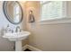 Cozy powder room with a pedestal sink, round mirror, and a window for natural lighting at 5825 Laurel Oak Dr, Suwanee, GA 30024