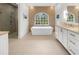 Bathroom featuring a soaking tub beneath a large arched window, stone accent wall, and white vanity at 4655 Jett Rd, Atlanta, GA 30327