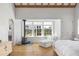 Bright bedroom featuring exposed beam ceilings, wood flooring, and a cozy fireplace with views of the outdoor landscape at 7455 Old Rico Rd, Chattahoochee Hills, GA 30268
