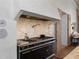Close up on a black gas range with a marble backsplash and custom vent hood at 7455 Old Rico Rd, Chattahoochee Hills, GA 30268