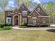 Stunning brick home boasts immaculate landscaping, arched entryway, and symmetrical design, nestled among mature trees at 6165 Lake Oak Lndg, Cumming, GA 30040