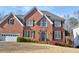 Two-story brick home with attached two-car garage, dormer windows, and mature landscaping on a bright day at 1023 Hawk Creek Trl, Lawrenceville, GA 30043