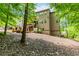 The backyard of this multi-story home features a sloping landscape, lush trees, and a brick foundation at 1351 Ashbury Park Dr, Hoschton, GA 30548
