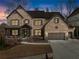 Beautiful brick home with a three-car garage and covered porch at dusk at 1351 Ashbury Park Dr, Hoschton, GA 30548