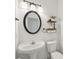Cozy powder room featuring pedestal sink, modern lighting, oval mirror, and rustic shelving for added storage and charm at 1811 Penny Nw Ln, Lawrenceville, GA 30043