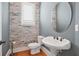 Elegant powder room featuring stone accent wall, pedestal sink, oval mirror, and wood flooring at 928 Boudreau Ct, Atlanta, GA 30328