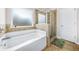 Bathroom features a large tub, glass enclosed shower, neutral tile, and a green rug at 6441 Oakhurst Pl, Fairburn, GA 30213