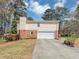 A house with cream vinyl siding, a brick base, and a large white garage door, accented with potted plants at 5221 La Paloma Sw Dr, Lilburn, GA 30047
