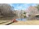 Scenic backyard featuring a serene pond view with two red Adirondack chairs on the lush green lawn at 1011 Dogwood Forest Ne Dr, Marietta, GA 30068
