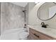 Modern bathroom features tiled walls, bathtub and shower combo, vanity with round mirror and marble countertop at 19 Grove Park Nw Pl, Atlanta, GA 30318