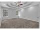 Large bedroom with neutral carpet, tray ceilings, ceiling fan, and natural light at 2551 Tolliver Dr, Ellenwood, GA 30294