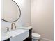 A well-lit powder room featuring a vessel sink, gold fixtures, marble countertop and round black mirror at 6110 Harvest Way, Cumming, GA 30028