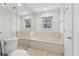Bathroom featuring a large tub with mirrored wall, plus a toilet, window and white walls at 3923 Ashford Lake Ne Ct, Brookhaven, GA 30319