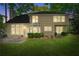 The backyard at night features green grass, mature trees and the lit back of the home with a chimney at 7045 Threadstone Overlook, Johns Creek, GA 30097