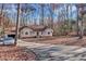 View of tan home with driveway and two car garage surrounded by tall trees in a wooded area at 9224 Snipe Ln, Jonesboro, GA 30236