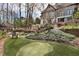 Landscaped backyard featuring a putting green, mature trees, stone retaining walls, and a relaxing seating area at 1025 Abingdon Ln, Johns Creek, GA 30022