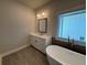 Bathroom featuring modern tub, stylish vanity, and tiled floors, complemented by natural light from the window at 161 Basil St, Cumming, GA 30040