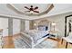 Spacious bedroom showcasing a tufted headboard, patterned bedding, tray ceiling with fan, and hardwood flooring at 1712 Green Farm Cir, Dacula, GA 30019