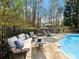 Outdoor stone patio with poolside lounge area and a lush backdrop of mature trees at 1544 Blue Bird Way, Cumming, GA 30041