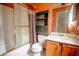 Orange bathroom featuring a shower-tub combo with glass doors, a toilet with dark storage and a sink with white counter at 2410 Deep Shoals Cir, Decatur, GA 30034