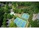 Wide aerial view of a sports complex with tennis courts, playground, and pool amid lush trees at 210 Chiswick Close, Johns Creek, GA 30022