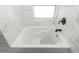 Close-up of a white bathtub with black hardware, marble tiling, and a small window at 1661 La France Ne St # 314, Atlanta, GA 30307