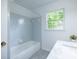 Bathroom with a white tub and shower, marble countertop, grey tiled floor and bright window at 5384 Blackhawk Dr, Acworth, GA 30102
