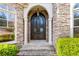 Close up of front door entrance with stone and black metal design and manicured bushes at 8069 Kenstone Ct, Sandy Springs, GA 30350