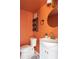 Vibrant powder room with orange walls, round gold mirror, and modern fixtures at 210 Trailmore Ct, Roswell, GA 30076