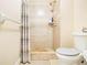 Shower stall with neutral tile, shower head, and glass shelves next to the toilet at 1472 Hartman Sw Dr, Lilburn, GA 30047