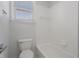 White bathroom with a toilet, and tub with white tiles and a window for ventilation and light at 7025 Bavarian Wood Pl, Buford, GA 30518