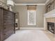 Bright bedroom with tan walls and a fireplace, featuring a large dresser, window, and neutral carpet at 275 Tynebrae Pl, Roswell, GA 30075