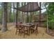 Outdoor dining area with a wooden table set under a shade sail surrounded by trees and nature at 240 Pinebrook Way, Roswell, GA 30076