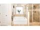 Bright bathroom featuring a soaking tub under a window and a glass enclosed shower with neutral toned tile surround at 910 Shannon Mist Dr, Loganville, GA 30052