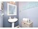 Elegant powder room featuring a pedestal sink, decorative mirror, and light blue accent wall at 910 Shannon Mist Dr, Loganville, GA 30052