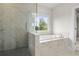 Modern bathroom featuring marble-like tiling, a glass-enclosed shower, and a separate soaking tub with a window view at 636 Silva St, Cumming, GA 30040