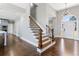 Inviting foyer with a wooden staircase, dark hardwood floors, and a view into a kitchen and front door at 525 James Lee Dr, Suwanee, GA 30024