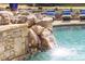 Close up of in-ground pool waterfall feature and stone surround with lounge chairs in background at 2335 Flat Stone Dr, Cumming, GA 30041