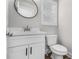 Clean half bathroom with white vanity, a round mirror, toilet, and window with modern fixtures at 6355 Akins Way, Cumming, GA 30041