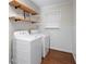 Convenient laundry room with white washer and dryer, open shelving, and hardwood floors at 608 Apache Trl, Woodstock, GA 30189