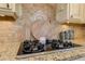 Close-up of granite counters and gas cooktop with mosaic backsplash and cream-colored cabinetry at 304 Gilmer Ct, Canton, GA 30115