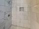 Close up of shower with marbled tile walls, recessed shelf and grey penny tile floor at 908 Kennesaw Dr, Forest Park, GA 30297