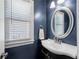 Stylish powder room featuring a dark blue wall, round mirror, vanity, and window at 3285 Millwood Se Trl, Smyrna, GA 30080