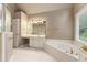 Bright bathroom featuring a large soaking tub, double vanity with white cabinets and gold fixtures, and a large window at 915 Summer Wind Pl, Roswell, GA 30075