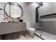 Modern bathroom with gray tiling, a round mirror above the sink, and a glass-enclosed shower with black fixtures at 8610 Sentinae Chase Dr, Roswell, GA 30076