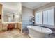 Bright bathroom features a soaking tub, vanity with a large mirror, natural stone flooring, and plantation shutters at 24 Ball Creek Hl, Atlanta, GA 30350
