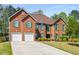 Attractive red brick home boasts an inviting driveway and well-maintained landscaping with green shutters, with a three-car garage at 308 Paper Woods Dr, Lawrenceville, GA 30046