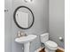 Powder room with modern fixtures including a pedestal sink, toilet and round mirror at 3986 Harmony Walk Se Way, Smyrna, GA 30082