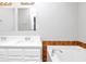 Bright bathroom featuring double sinks, white cabinets, and a tub with brown tile accents at 3052 Sw Highbury Sw Trl, Atlanta, GA 30354