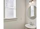 Bright powder room featuring a pedestal sink, round mirror, and natural light from the window at 2240 Mulsanne Dr, Lithonia, GA 30058